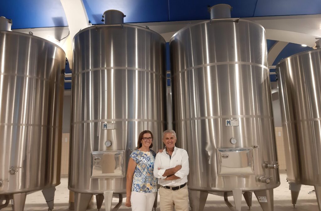 A sinistra del lettore Marisa Cuomo, in maglietta azzurra a motivi Moda Mare Positano, con il marito Andrea Ferraioli in camicia bianca sulla destra: sullo sfondo ci sono quattro cisterne della Cantina Marisa Cuomo per produrre vino in Campania